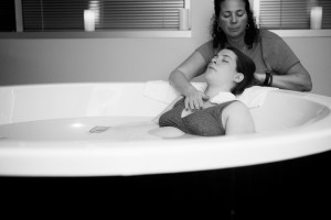 Ursula supporting a laboring woman in a tub