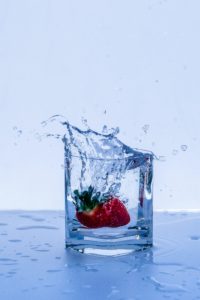 A strawberry being dropped into a glass of wter