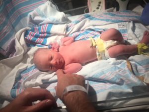 Newborn baby getting newborn exam, holding dad's finger 