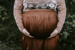 A full figured woman holding her pregnant belly in a brown skirt 