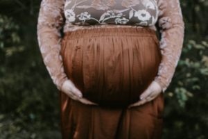 A full figured woman holding her pregnant belly in a brown skirt