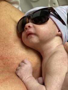 Newborn held on chest in hat and sunglasses