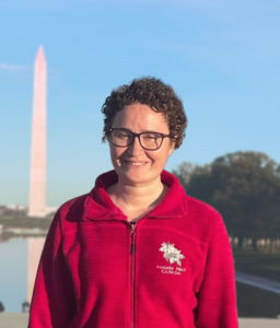 Woman with short curly hair, glasses, in a red top standing at the national mall