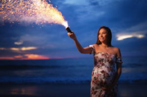 Pregnant woman in a floral dress holding out a sparkler 