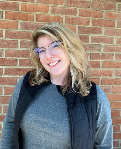 Blonde woman with glasses in a grey shirt and black vest 