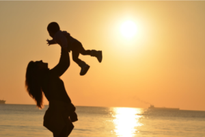 woman tossing baby in the air against a sunset 