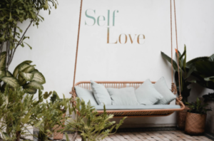 Swing amongst plants with the words Self Love on the wall behind it 