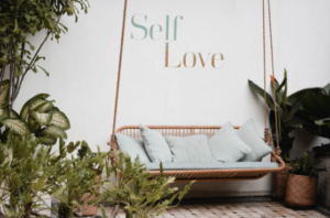 Swing amongst plants with the words Self Love on the wall behind it