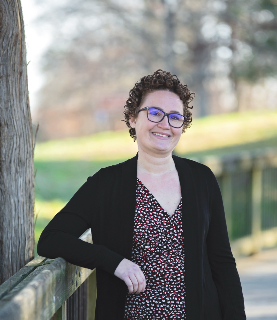 Woman with short curly hair, glasses in a dress with a black cardigan 