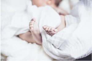Newborn asleep with toes sticking out of a white blanket
