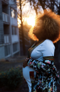 African American woman backlit by a sunset as she cradles her belly.