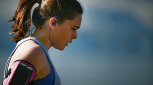 brunette woman in blue tank top and ear buds working out 