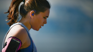 brunette woman in blue tank top and ear buds working out