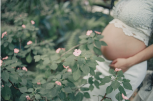 Woman in a white 2 piece, wither her belly exposed surround by pink flowers 
