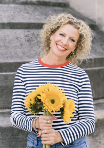 Curly blonde woman wearing stripes holding a bouquet of sunflowers