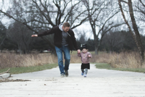 Man in sweatshirt running on a board walk holding a young girls hand