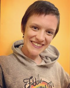 caucasian woman with short brown hair in a hooded shirt on an orange background