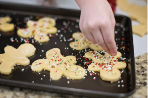 a child's hand putting sprinkles on cookie cutouts