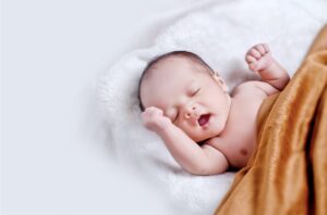 Newborn on white blanket with an orange blanket draped over their chest.  