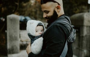 Bald man with a beard baby wearing a young child in a white snow suit