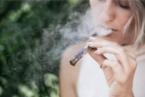 A blond woman in a white shirt smoking marijuana 