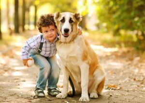 A boy in suspenders hugging a mixed breed dog 